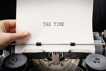 Tax Concept. Hand working on an old typewriter with paper, close up