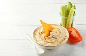 Ceramic bowl of tasty hummus with chips and vegetables on table