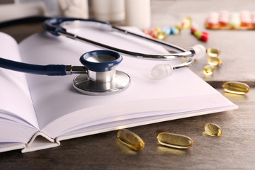 Stethoscope with open book and pills on wooden background. Medical literature concept