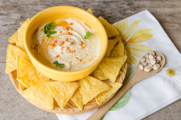 Hummus and corn chips, on wood table.
