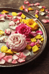 Pink and yellow rose petals in silver bowl with water on wooden background
