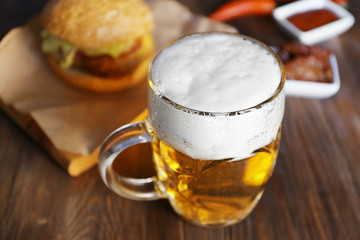 Glass mug of light beer with snacks on dark wooden table, close up