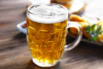 Glass mug of light beer with snacks on dark wooden table, close up