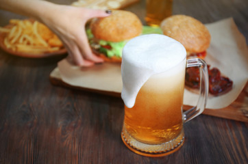 Glass mug of light beer with snacks on dark wooden table, close up