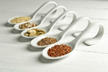 Different kinds of seeds in spoons on wooden table