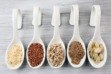 Different kinds of seeds in spoons on wooden table