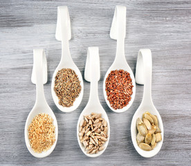Different kinds of seeds in spoons on wooden table