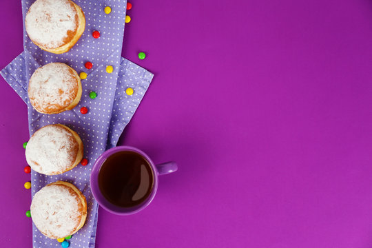 Delicious donuts with powdered sugar and cup of tea on purple surface, top view
