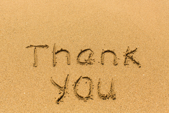 Thank you - inscription by hand on golden beach sand.