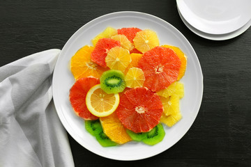 Plate of fresh peeled and sliced citrus on wooden background, top view