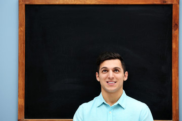 Attractive young man against blackboard.