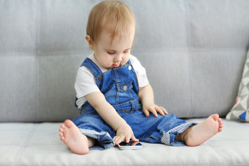 Fototapeta premium Baby sitting on sofa and playing with smartphone