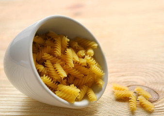 Dry fusilli pasta in white bowl on wooden table