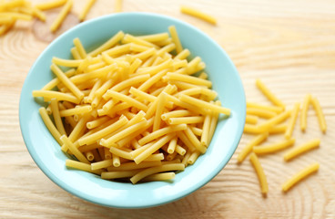 Dry maccheroni pasta in blue plate on wooden table