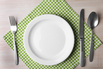 Empty plate with silver cutlery and napkin on wooden table, top view