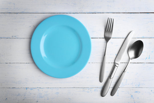 Empty plate with silver cutlery on wooden background