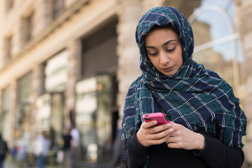Young woman wearing hijab in city texting on cell phone - obrazy, fototapety, plakaty