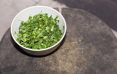 The chopped herbs on the plate stands on a stump. Parsley, dill and coriander in a white plate. 