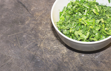 The chopped herbs on the plate stands on a stump. Parsley, dill and coriander in a white plate. 