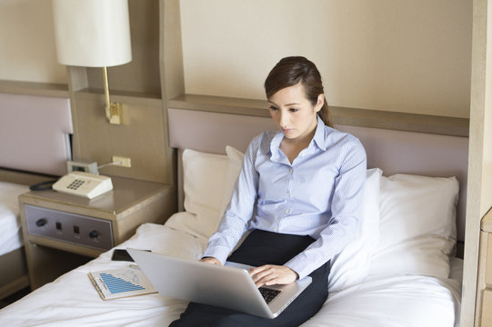 Women have to work on a laptop sitting on a bed in a hotel room