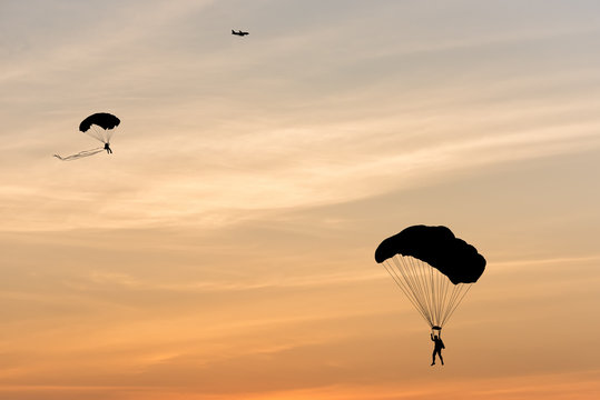 Silhouette of parachute and airplane on sunset background