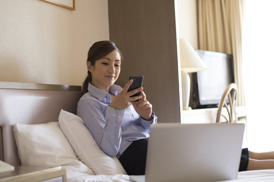 Women sat in business hotel bed, looking at the smartphone