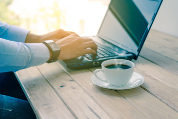 Coffee cup with closeup man typing a laptop on wooden table.