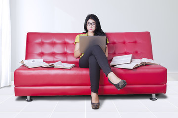 Woman uses laptop with books on sofa