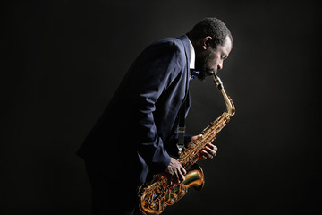 African American jazz musician playing the saxophone on grey background - obrazy, fototapety, plakaty