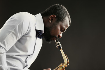 African American jazz musician playing the saxophone on grey background