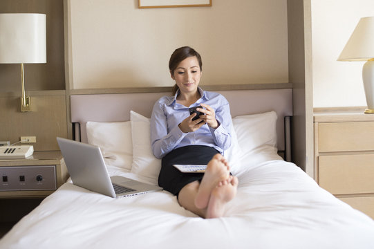 Women sat in business hotel bed, you are sending e-mail on your smartphone