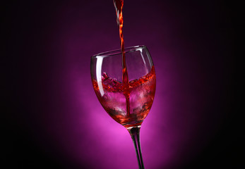 Wine pouring in glass on dark purple background