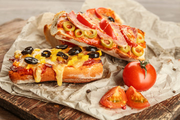 Hot pizza baguettes with olives, tomatoes and ham on wooden table