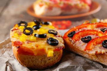 Hot pizza baguettes with olives, paprika, ham and salami on wooden table
