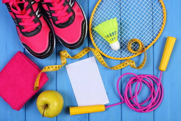 Pink sport shoes, fresh apple and accessories for sport on blue boards, copy space for text on sheet of paper