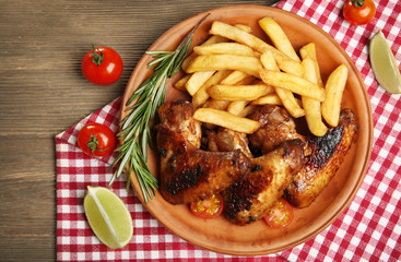 Baked chicken wings with French fries on brown plate