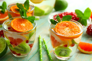 Refreshing cocktails with ice, mint, pomegranate seeds and slices of fruits on blue wooden background