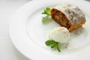 Slice of strudel with apples, walnut, raisins and ice cream ball on white plate