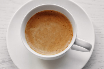 Cup of coffee on light wooden background, top view