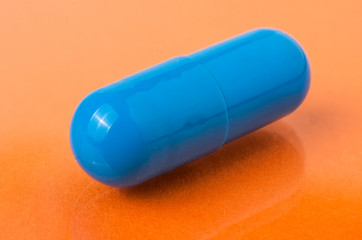 one blue pills on an orange background close-up macro