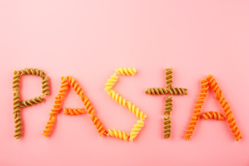 Pasta word made of varicolored fusilli on pink background