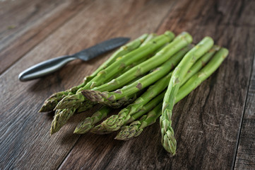 Closeup shot of fresh asparagus bunch with kitchen knife aside on wooden rustic background