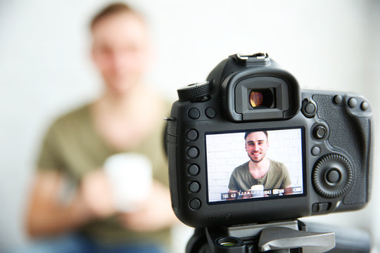 Young male blogger with cup of tea on camera screen