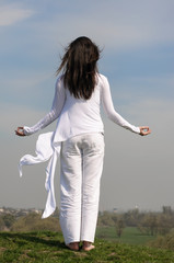 Girl meditates on a hill against the blue sky.