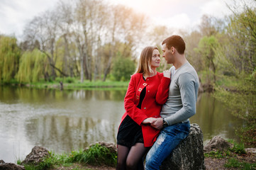 Happy loving couple sitting and hugging on stone at park backgro