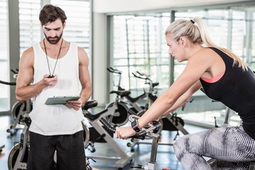 Trainer looking at stopwatch and woman using exercise bike