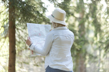 Fototapeta premium Young feYoung woman sitting with paper map near the car in the f