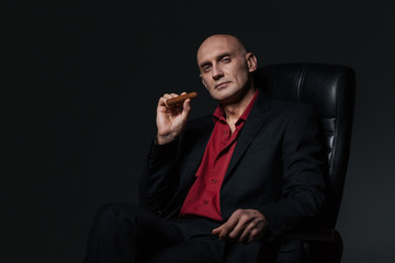 Confident handsome businessman sitting in office chair and smoking cigar