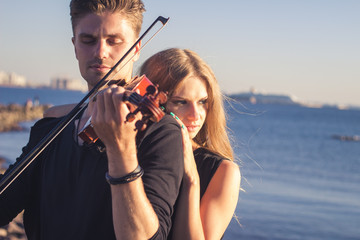 Beautiful couple violinist and young woman together near sea bay