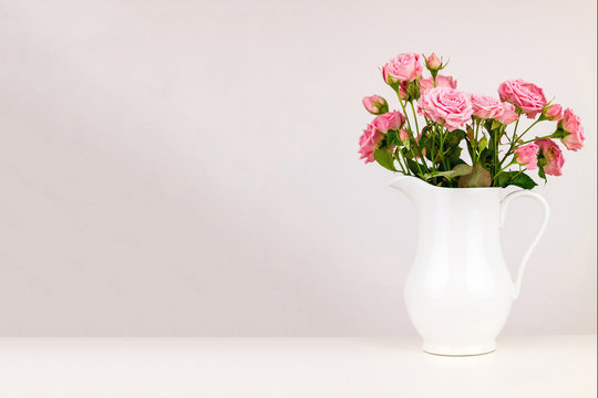 Pink flowers in white jug. Roses in jug.